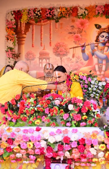 A sant being garlanded on stage